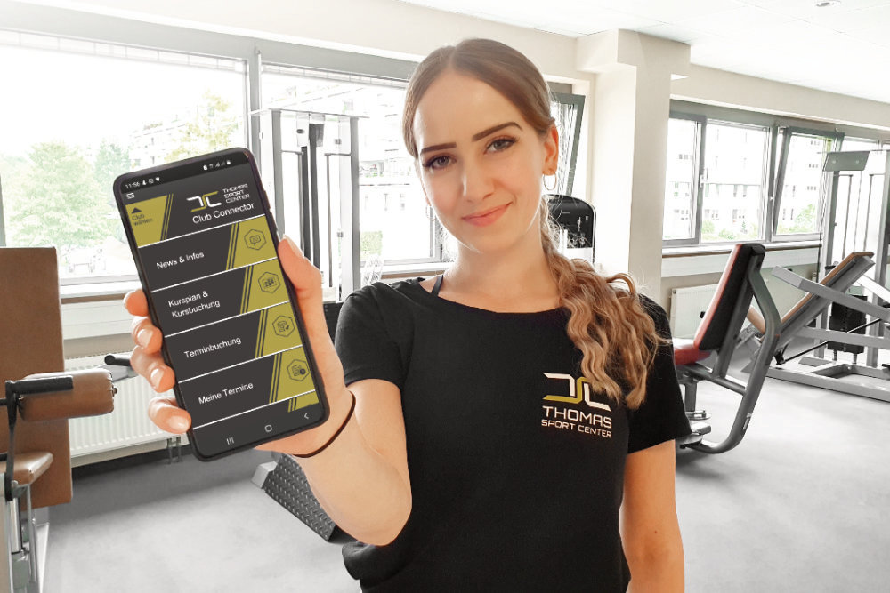 Mitarbeiterin zeigt die Clubconnector App des Thomas Sport Centers auf dem Smartphone
